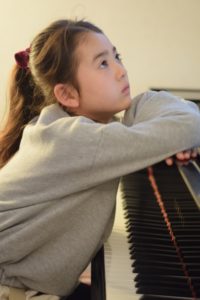 ピアノの前で上を見上げる女子